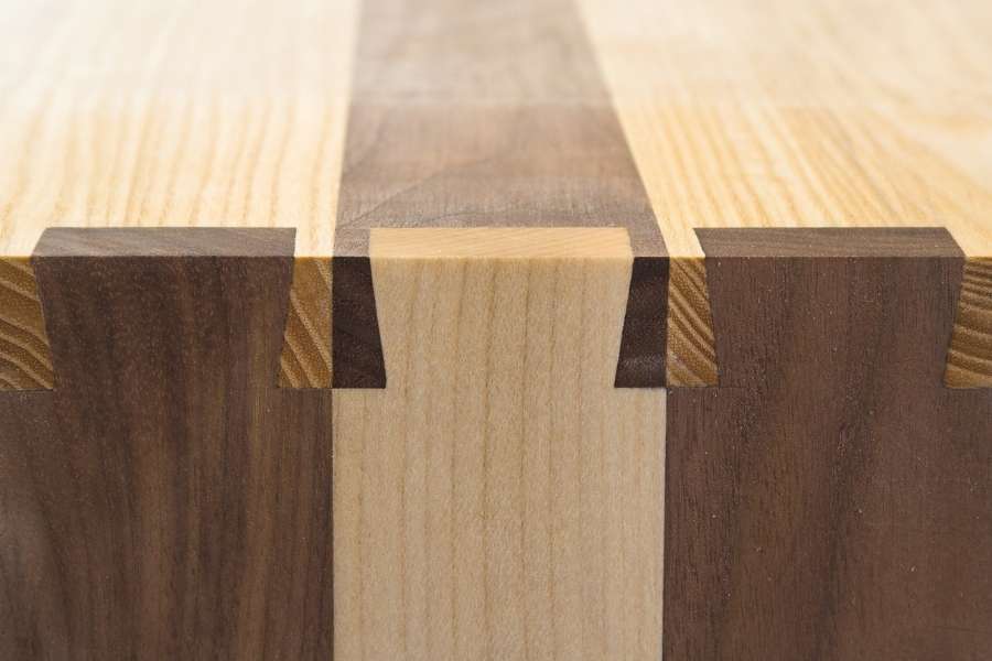 Close-up of a precise dovetail joint connecting light and dark wood pieces with interlocking pins and tails.