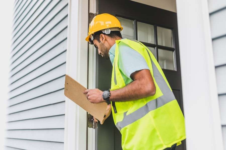A professional inspector wearing a hard hat and high-visibility vest conducting a detailed home inspection at a doorway.