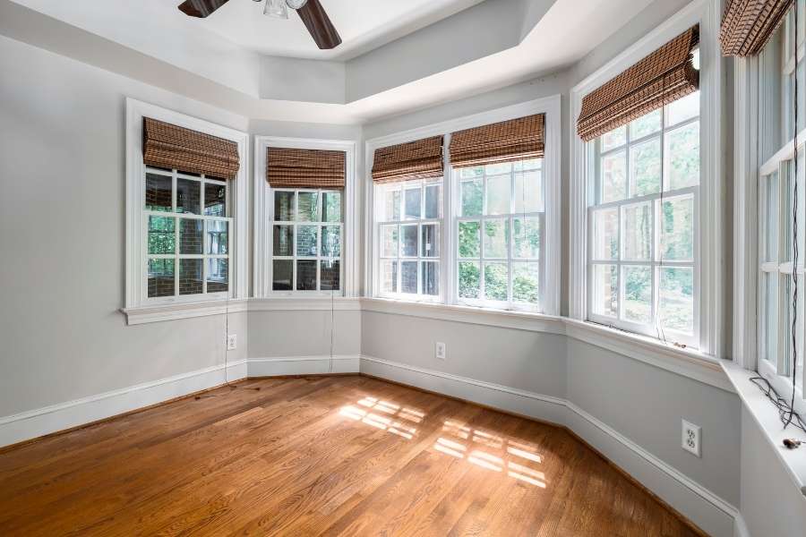 A bright room featuring a bay of energy efficient windows with wooden blinds and hardwood floors.