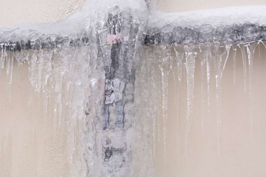 Thick icicles hanging heavily from an outdoor frozen pipe system during freezing winter weather.