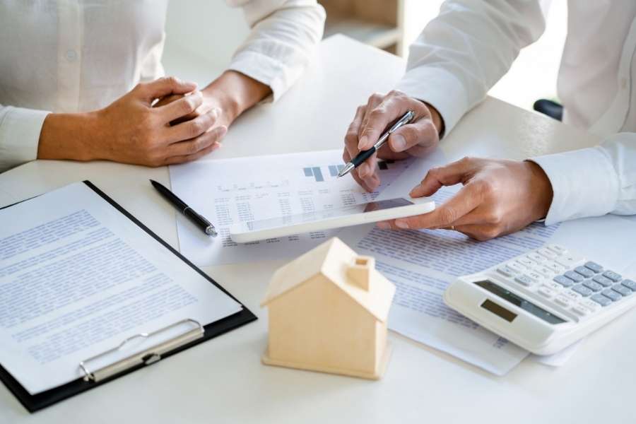 Financial advisors reviewing property documents and a model house to decide whether to buy or keep renting.